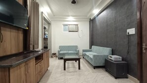 A living room with a TV, sofas, a coffee table, and a small table with a projector. - 85 The Ganges 2 Bhk Apartment for Homestay (Rishikesh)