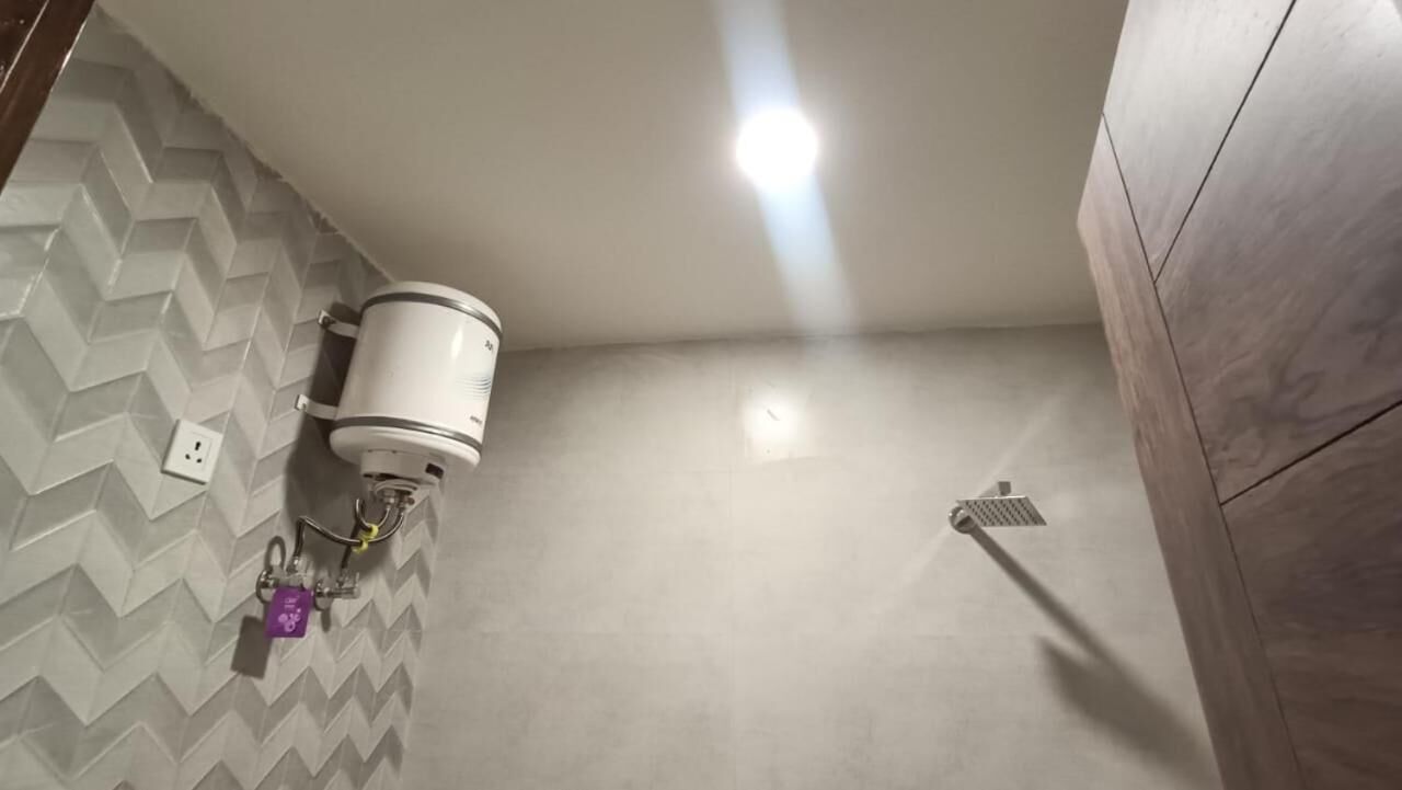 Un baño con inodoro blanco, calentador de agua instalado en la pared y zona de ducha.
