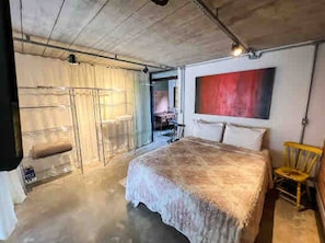 Un dormitorio con una cama grande, una silla y un cuadro abstracto rojo en la pared.