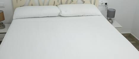 Un letto con testiera in legno, biancheria bianca e un comodino con una lampada.