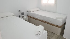 Une petite chambre propre, avec deux lits, une table de chevet avec une lampe et une fenêtre avec des stores.