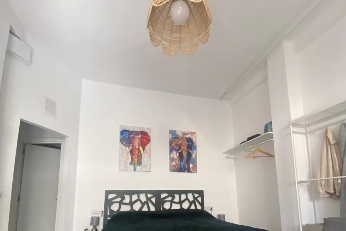 Een slaapkamer met een bed, een slaapbank, een hanglamp en twee aan de muur bevestigde schilderijen.