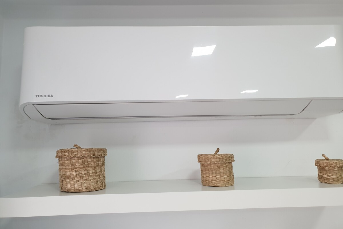 A white air conditioning unit labeled 'TOSHIBA' mounted on a wall with three wicker baskets on a shelf below.
