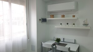 Une pièce lumineuse et moderne, avec une table et des chaises blanches, une petite plante en pot et des objets décoratifs disposés sur des étagères.