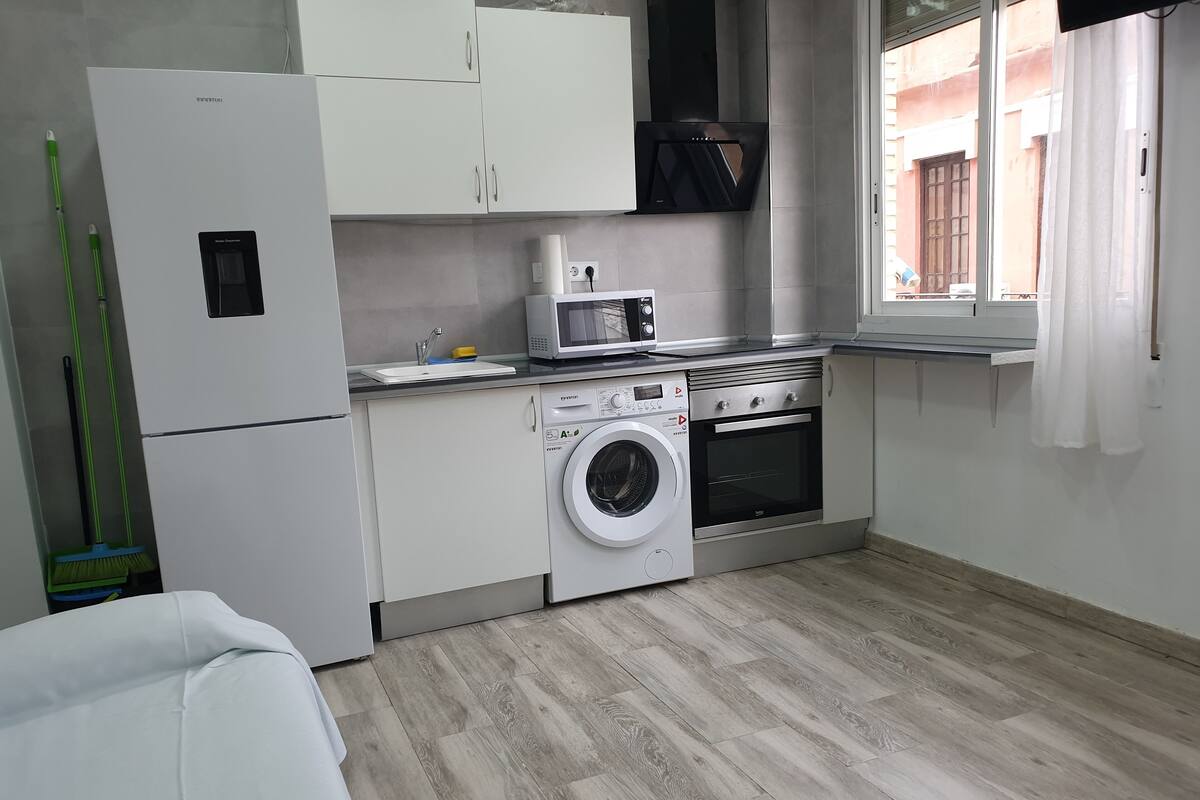 Een kleine keuken met een wasmachine, oven, magnetron en kastjes.