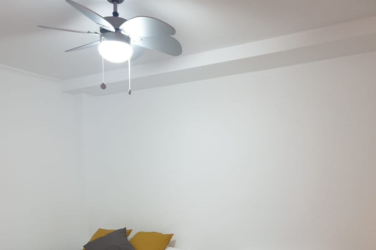 A hotel room with two single beds, a ceiling fan, and a nightstand with a lamp.