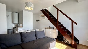 A modern living room with a sofa, a staircase, a radiator, and a dining area.