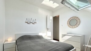 A bedroom with a bed, bedside tables, a desk, a chair, a skylight, and wall decor.