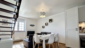 A modern kitchen with white cabinets, a dining area with a white table and chairs, and a staircase with dark wood railings.