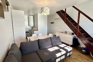 A modern living space with a sofa, dining table, kitchenette, and a staircase.