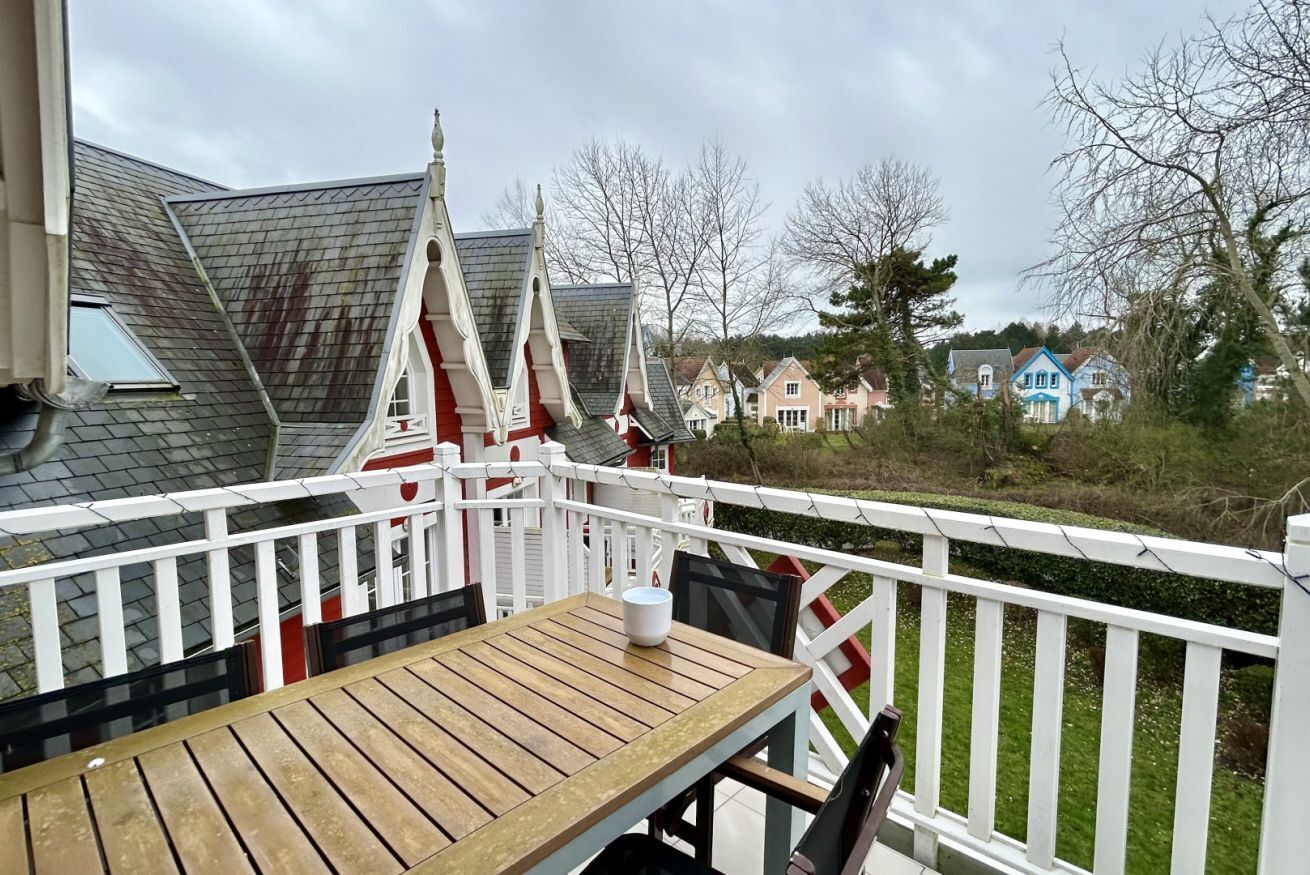 Eine Holzterrasse mit Tisch und Stühlen, weißen Geländern und Blick auf die Nachbarhäuser.