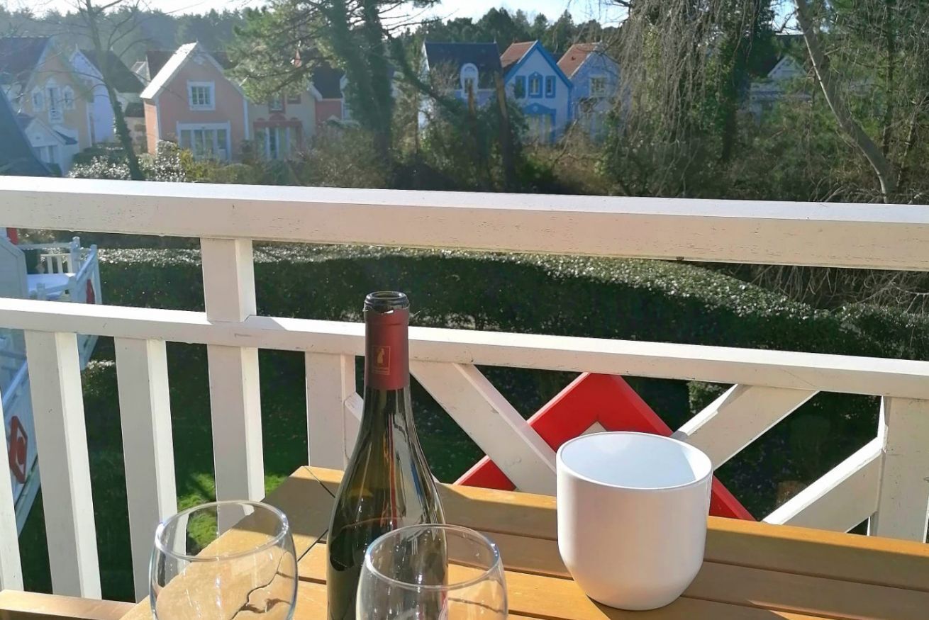 Eine Holzterrasse mit weißer Brüstung, eine Weinflasche und zwei Gläser auf einem Tisch.
