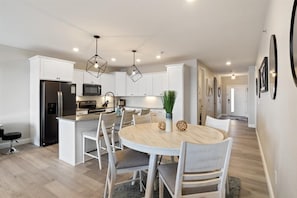 Una cocina moderna con armarios blancos, una isla central y un comedor con sillas.