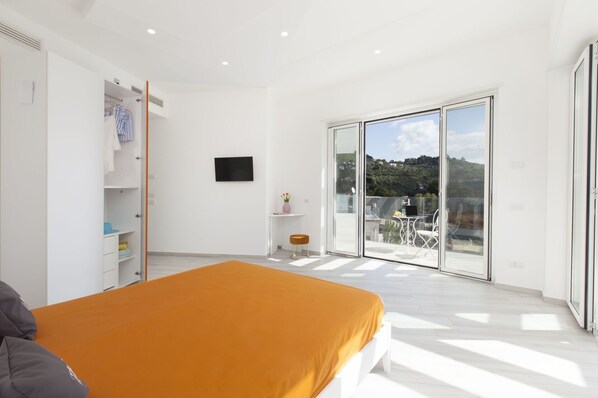 A bedroom with a bed, a wardrobe, a TV, a small table with a vase, and a balcony with a table and chairs.