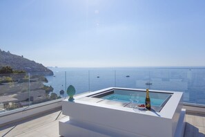 A modern outdoor hot tub with a clear view of the sea and a distant island.