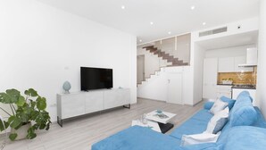 Un salon moderne avec un téléviseur à écran plat, un canapé bleu et un escalier menant à la cuisine.