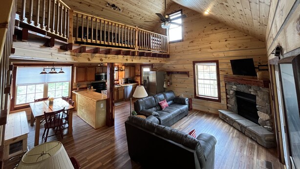 A spacious cabin with a wooden interior, a dining area, a living room with a fireplace, and a balcony with a railing. - Riverfront Cabin: The Cozy Southern Brook Trout Lodge  (Luzene)