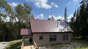 A cabin with a metal roof, a wooden deck, and a gravel path leading to the entrance. - Riverfront Cabin: The Cozy Southern Brook Trout Lodge  (Luzene)