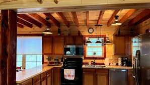 A kitchen with wooden cabinets, a black stove, stainless steel appliances, and pendant lights. - Riverfront Cabin: The Cozy Southern Brook Trout Lodge  (Luzene)