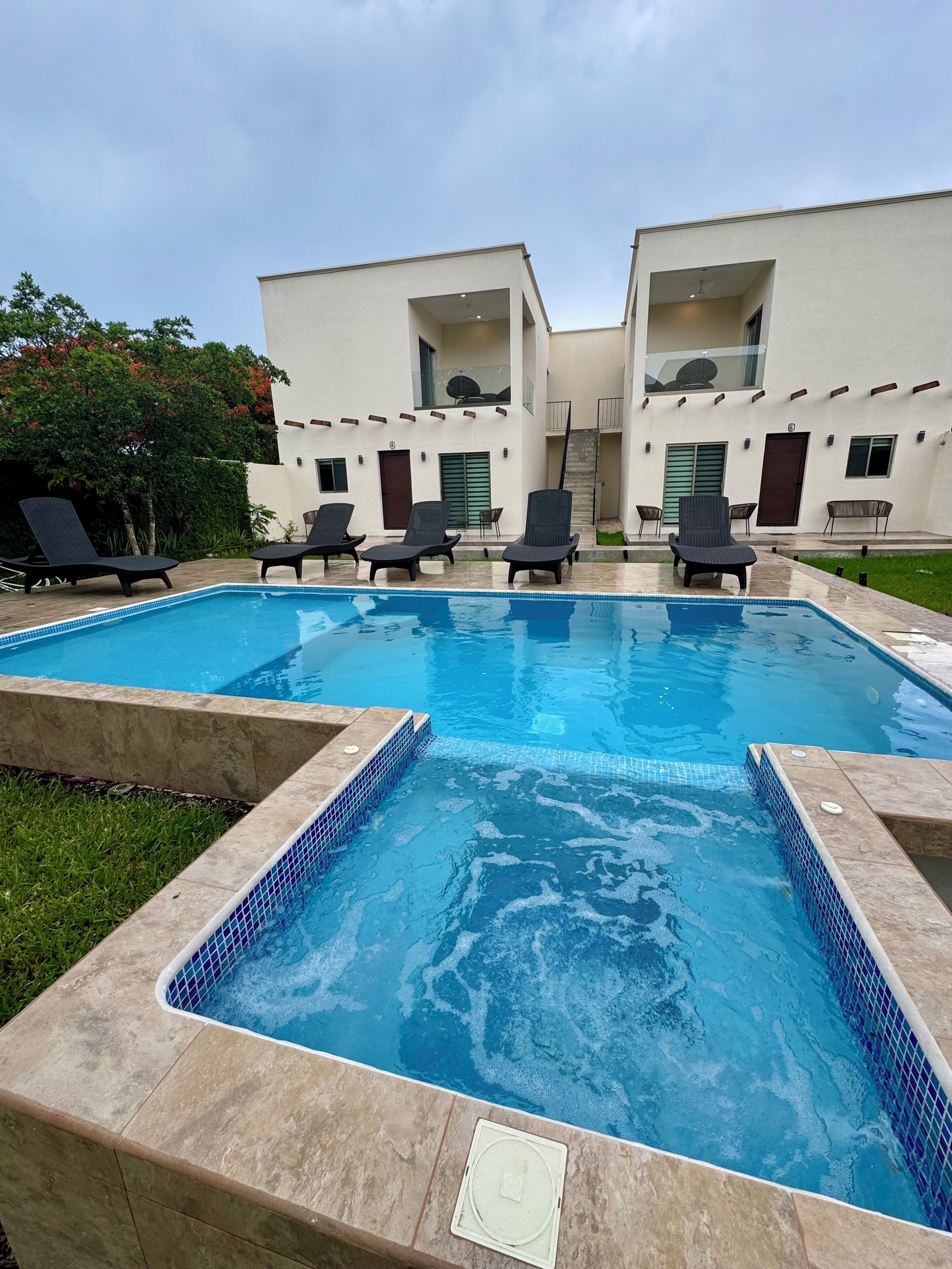 A swimming pool with lounge chairs and a modern building with balconies.