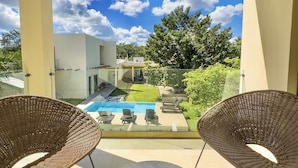 Ein Balkon mit zwei Korbstühlen, einem Marmortisch und Blick auf ein Schwimmbecken und Grünflächen.