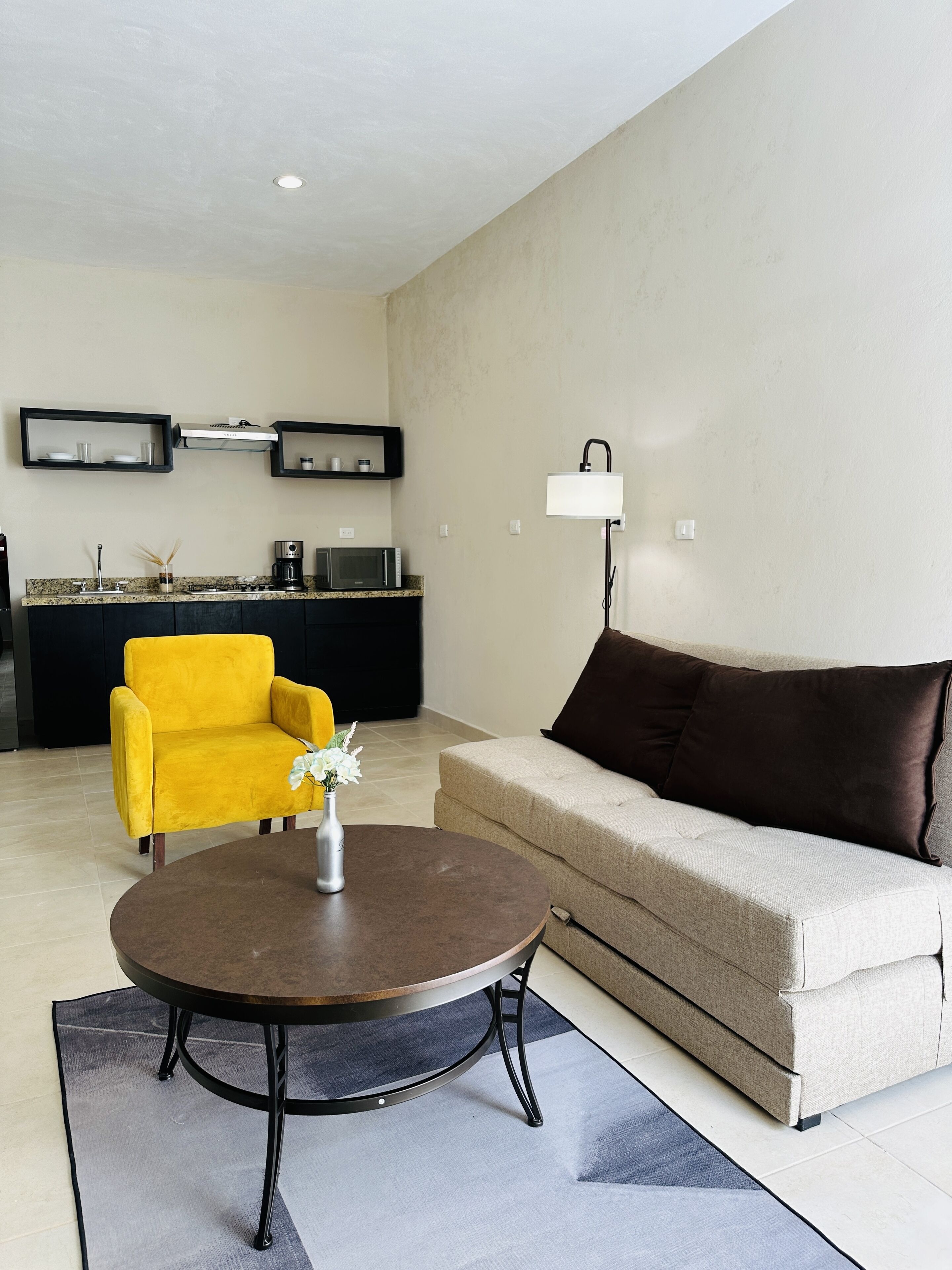 A modern living room with a sofa, a yellow armchair, a round coffee table, and a kitchen area in the background.