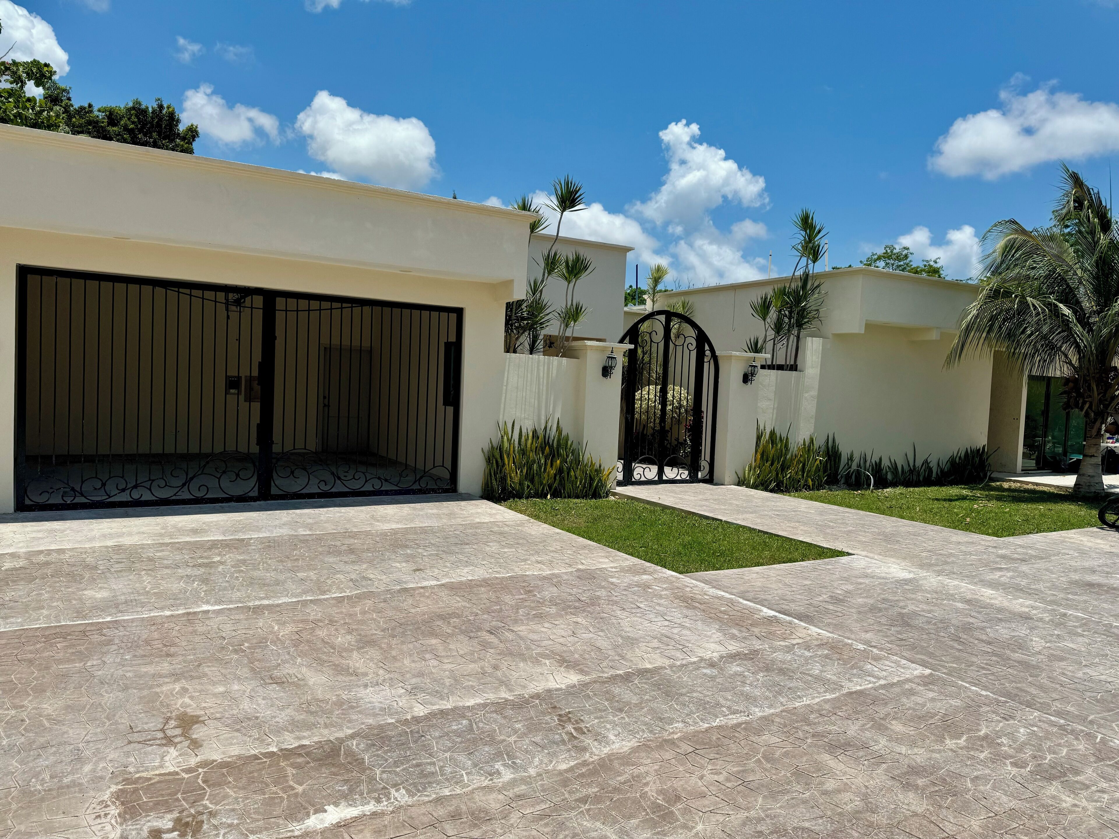 Una casa moderna con un garaje amplio, un camino de entrada cerrado por una reja y un césped bien cuidado.