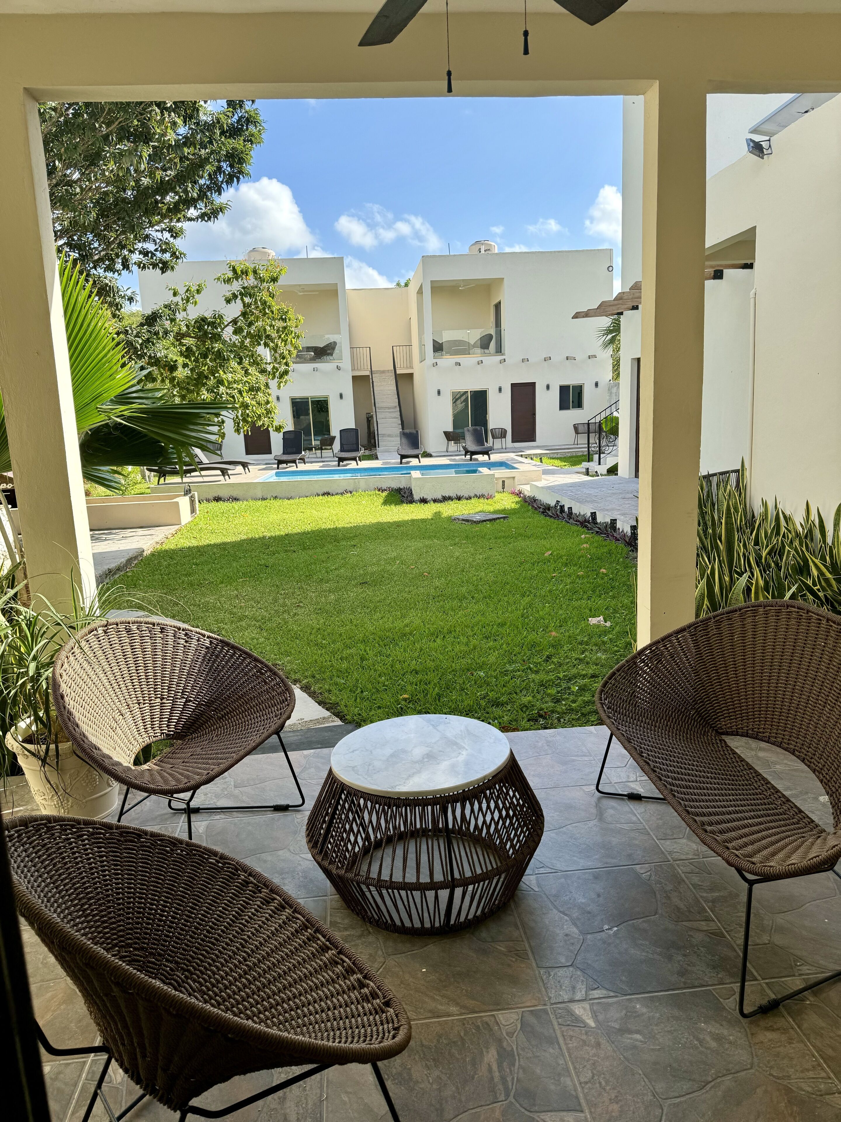 Un patio con sillas de mimbre y una mesa de mármol, con vistas a una piscina y un césped cuidado.