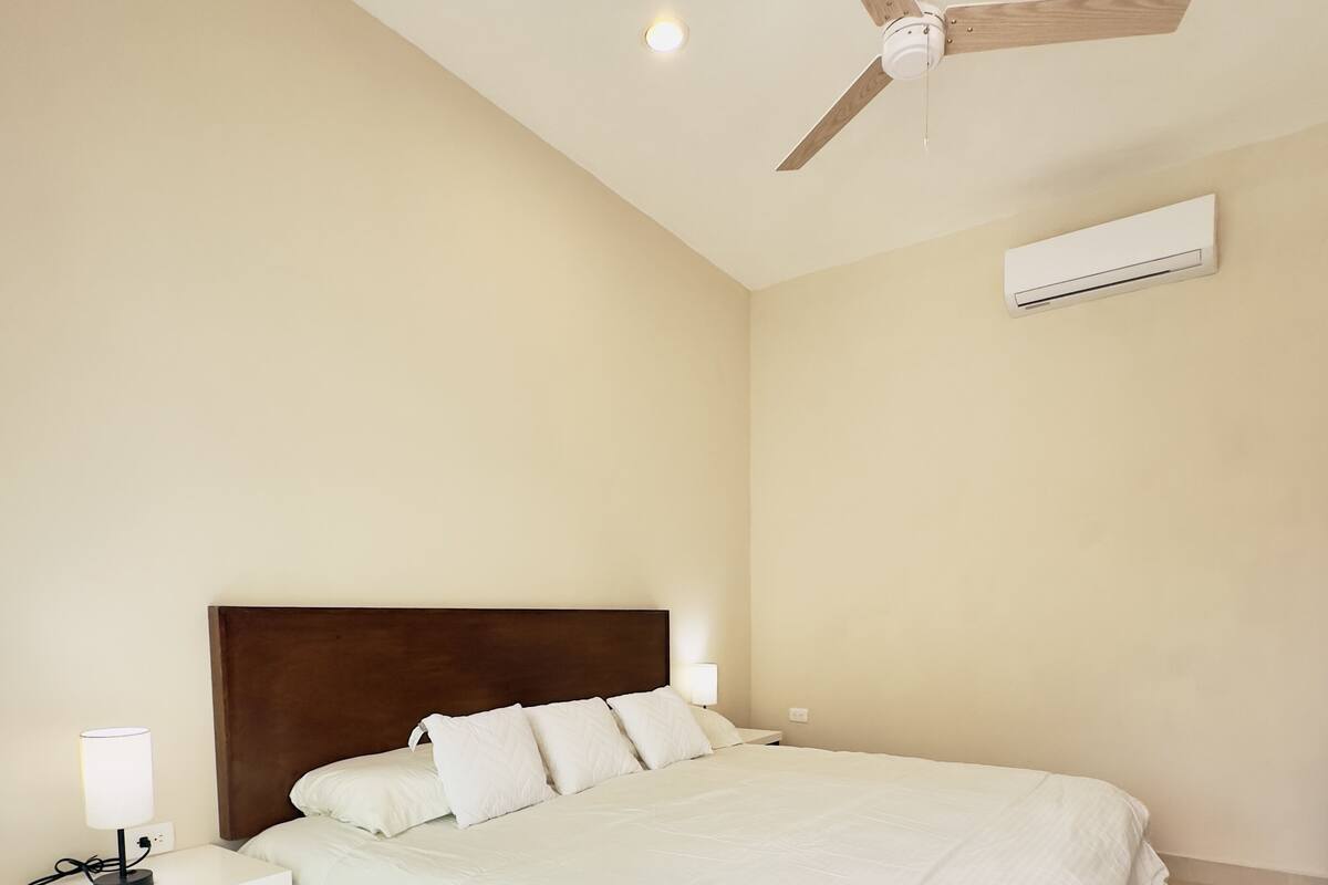 Ein Schlafzimmer mit Bett, Nachttisch, Lampe, Deckenventilator und Klimaanlage.