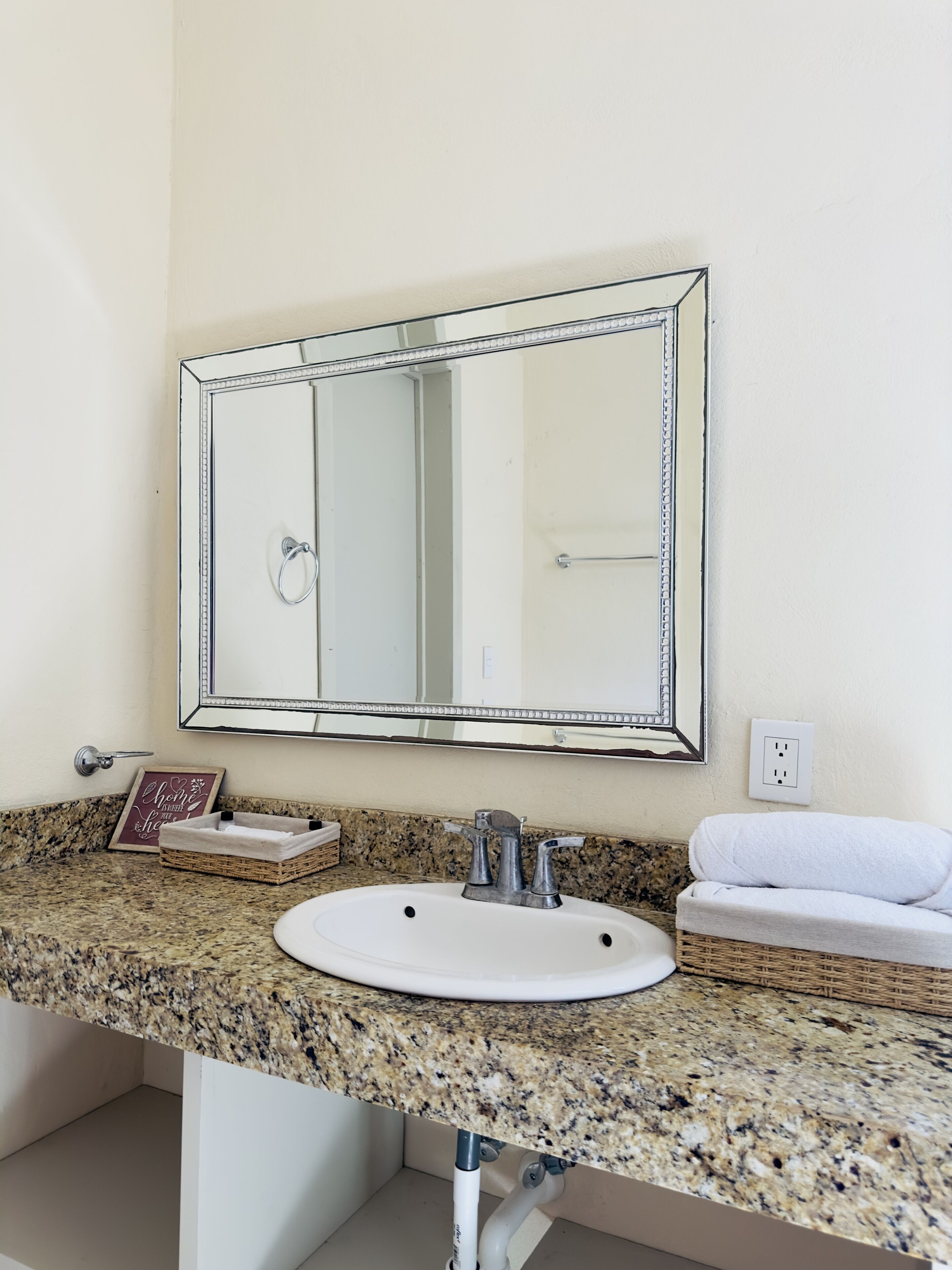 A bathroom with a granite countertop, a white sink, a mirror, and a towel rack.