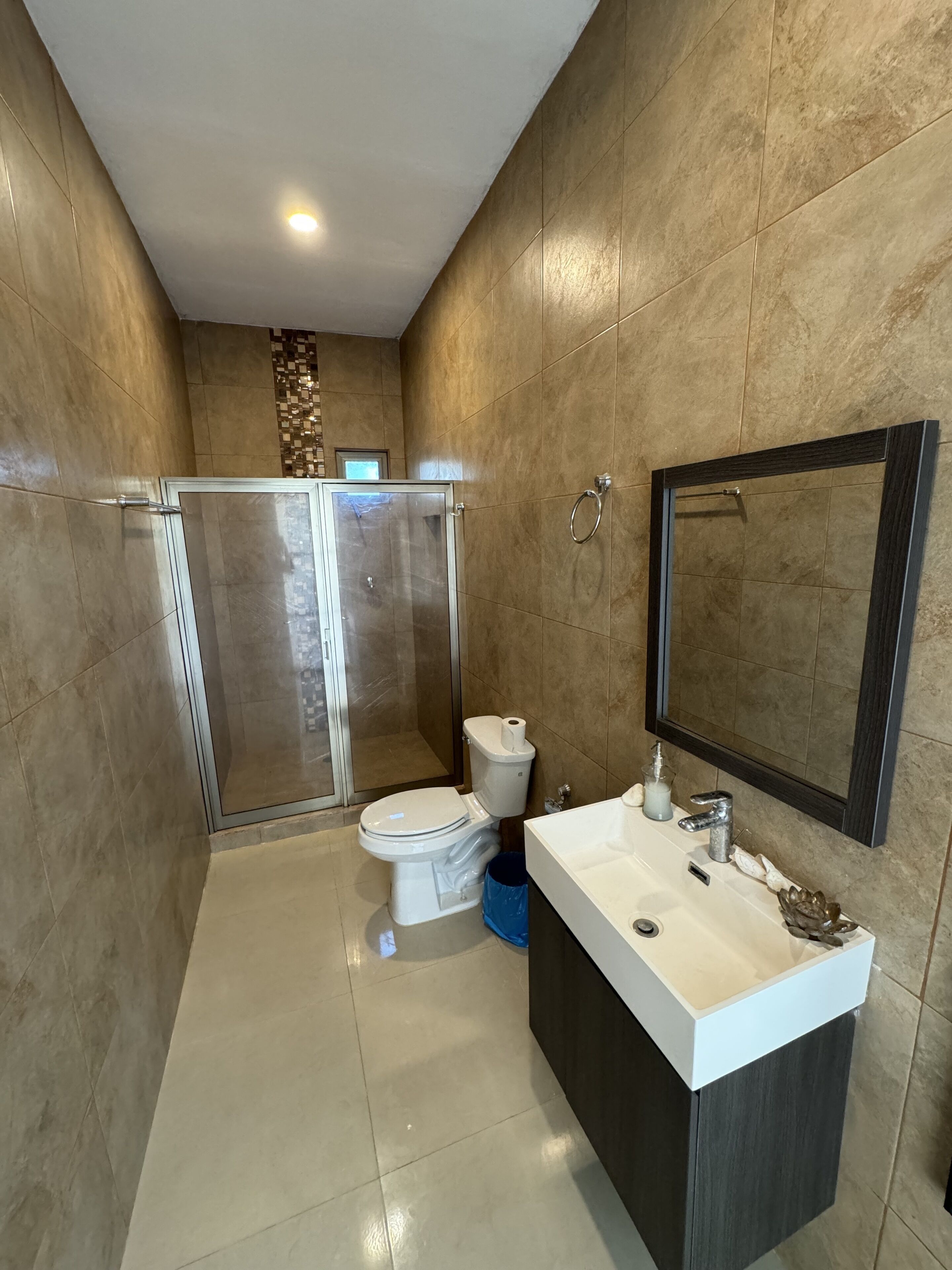 Une salle de bain moderne avec une douche à parois de verre, des toilettes, un lavabo avec un miroir et un sol carrelé.