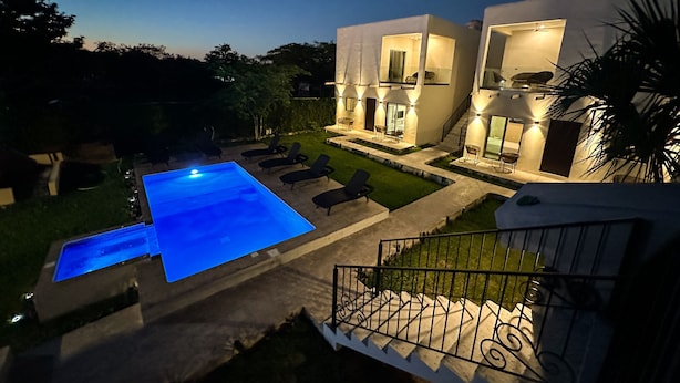 Ein modernes Haus mit Schwimmbad, Sitzgelegenheiten im Freien und einer gut beleuchteten Terrasse.
