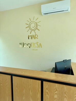 A reception desk with a wall-mounted air conditioner and a decorative wall sign that reads "MAR TURQUESA VILLAS".