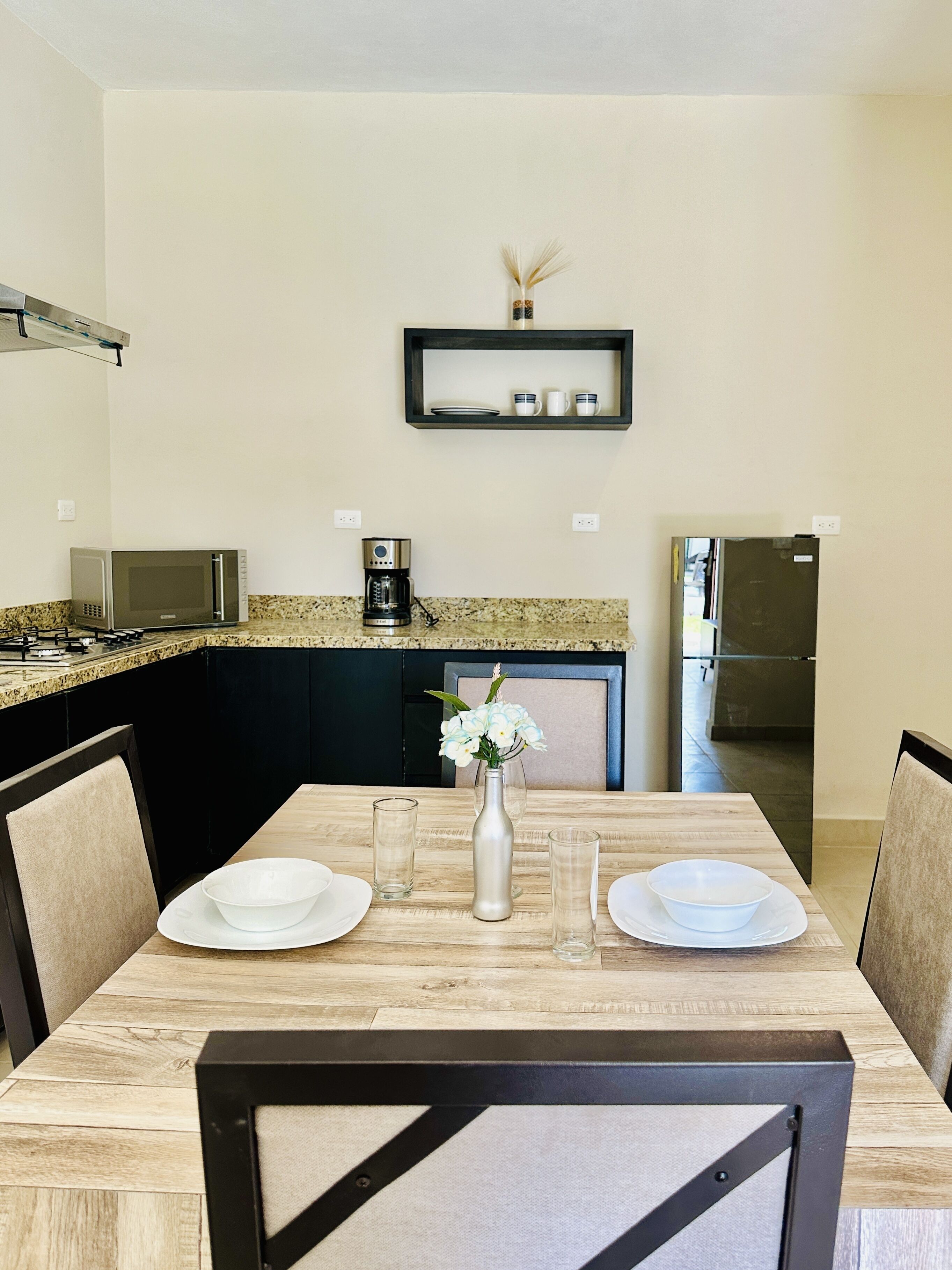 Uma cozinha moderna com uma mesa de jantar posta para dois, uma cafeteira e um micro-ondas.