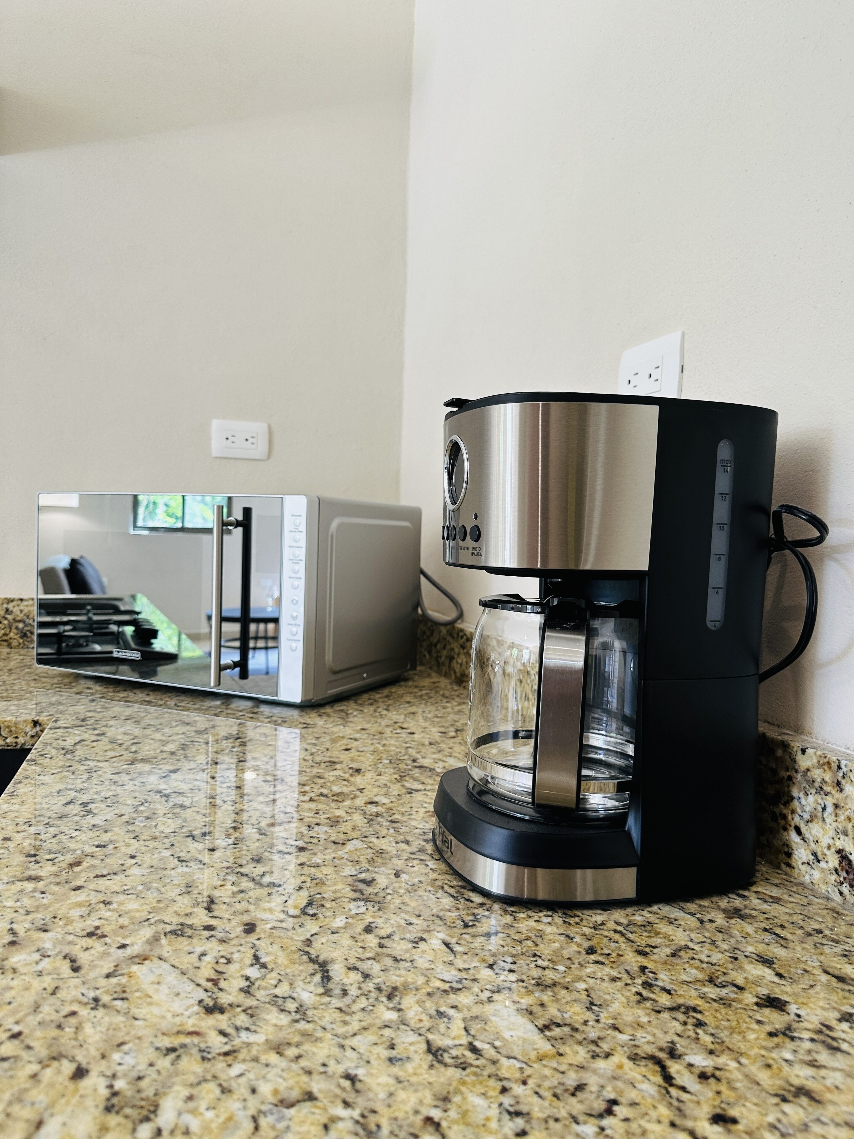 Une machine à café et un four à micro-ondes sont posés sur un plan de travail en granit.