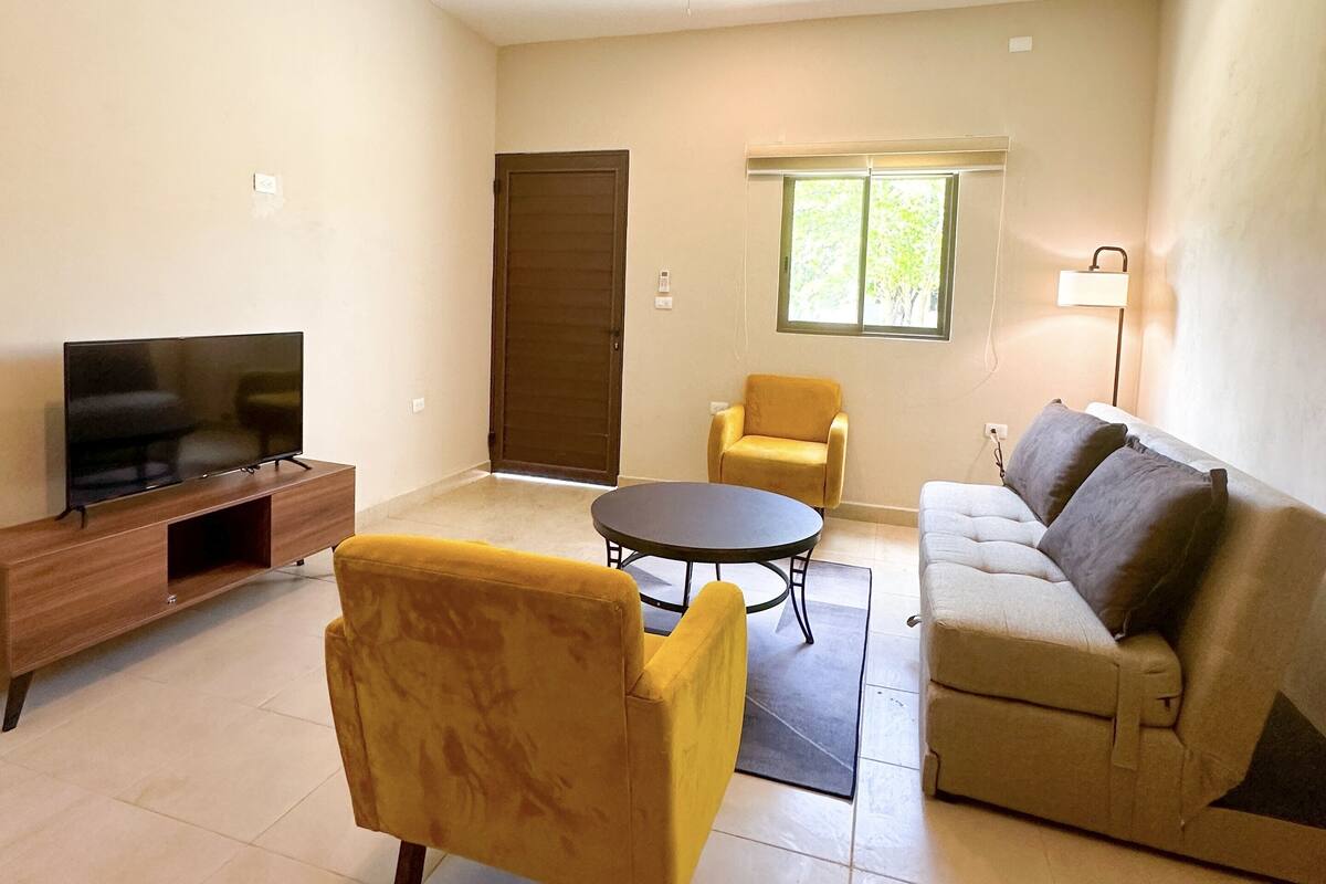 Ein Wohnzimmer mit Sofa, Sessel, TV-Standfuß und Deckenventilator.