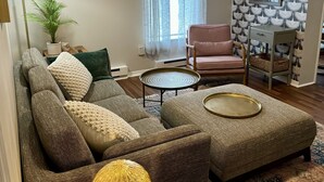 Ein Wohnzimmer mit einem Ecksofa, einem kleinen runden Tisch, einer Stehlampe und einer Wand mit Muster.