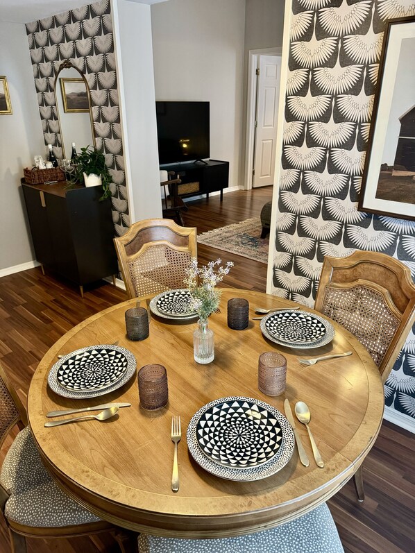 A dining area with a round wooden table set for four, featuring black and white patterned plates and silverware.