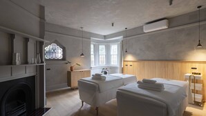 Une chambre avec deux lits, une cheminée, une fenêtre ornée de vitraux et un mur en bois.