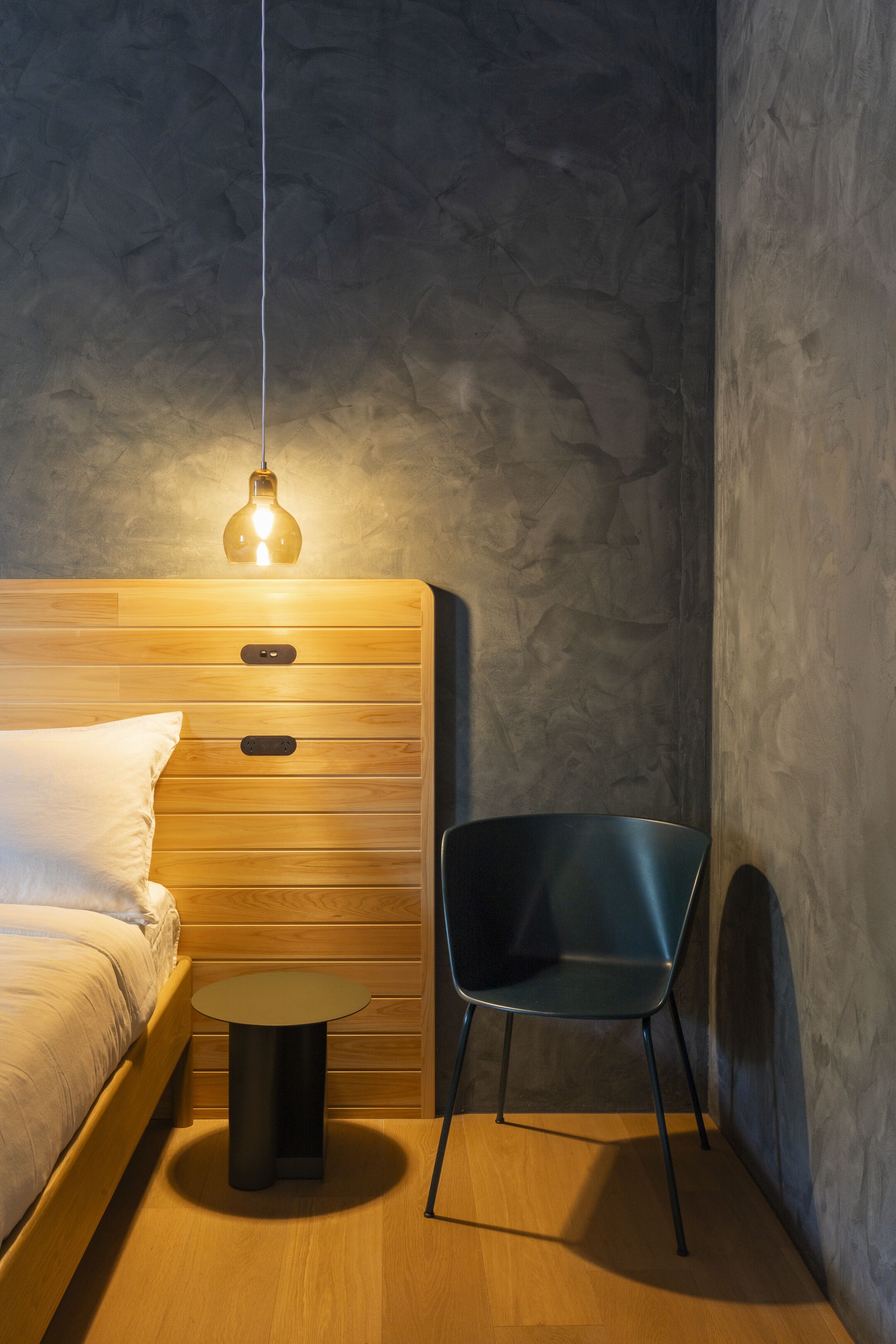 Un dormitorio con cama de madera, una mesita de noche, una silla y una lámpara colgante.