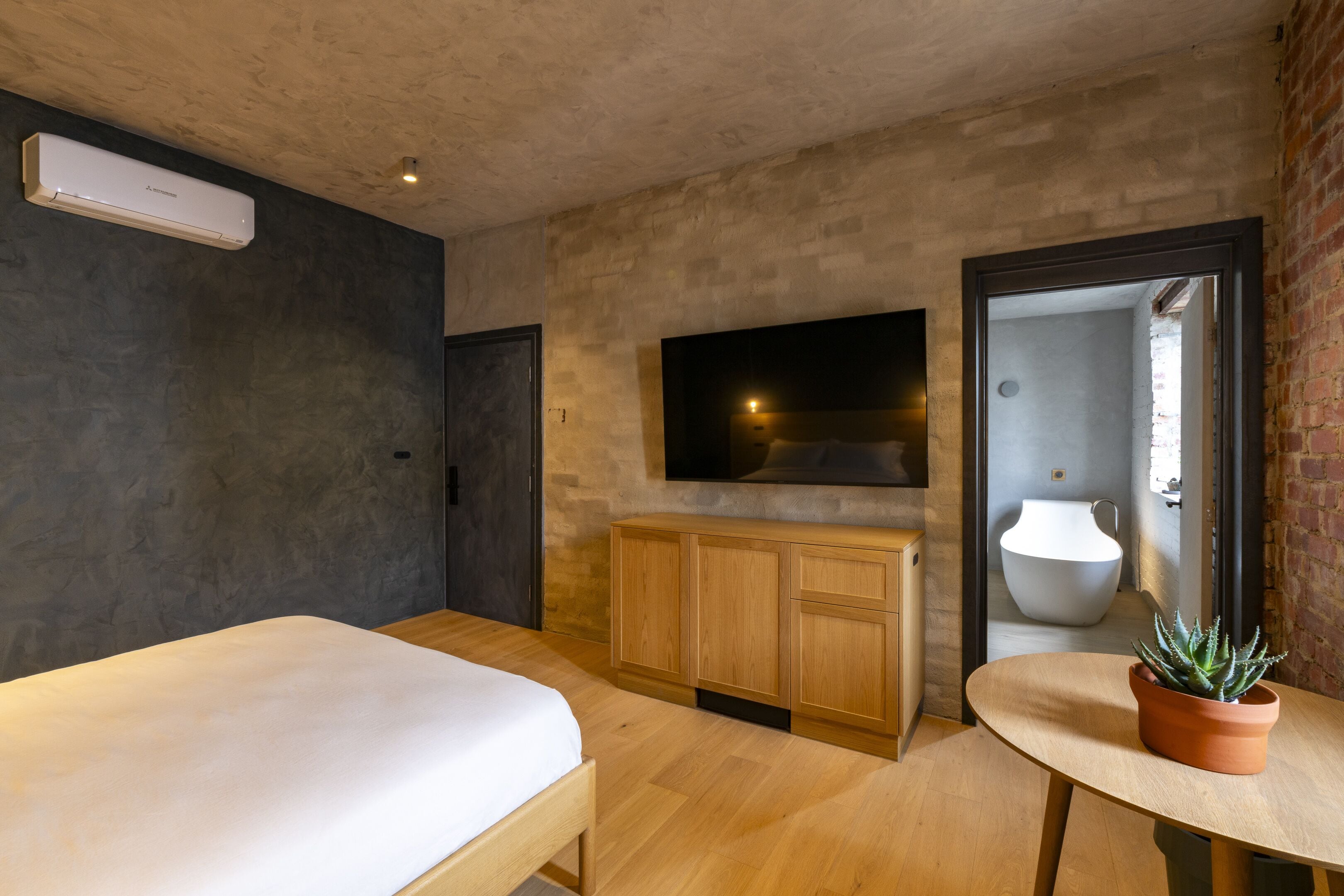Quarto moderno com cama, armários de madeira, televisão e planta em vaso.