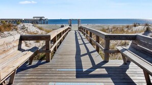 A wooden boardwalk leading to a beach with a pier in the background. - Great Summer Rates 1B 1B South beach-Steps to pool-beach-restaurants-nightlife! (Tybee Island)