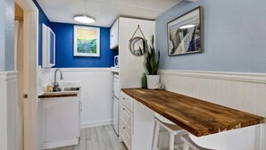 A compact kitchen with white cabinetry, a wooden countertop, and a hanging mirror. - Great Summer Rates 1B 1B South beach-Steps to pool-beach-restaurants-nightlife! (Tybee Island)