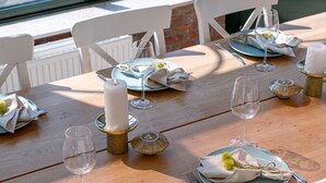 A dining table set with white chairs, plates, cutlery, and candles.