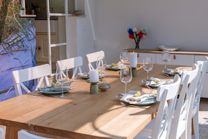 Una mesa de comedor de madera dispuesta con sillas blancas, platos, vasos y una vela.