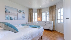 A bedroom with a bed, a dresser, a nightstand, and a window with curtains.