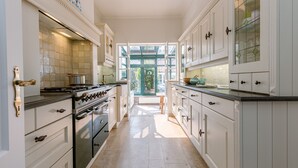 A kitchen with white cabinetry, a stove, and a view through an open door to a garden.