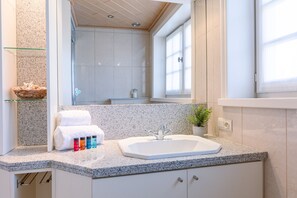 Un baño moderno con encimera de granito, lavabo blanco y cabina de ducha con mampara de vidrio.