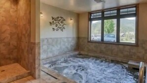 Ett spaområde med ett bubbelbad, stenmurar, en dekorativ väggdekoration och ett fönster med utsikt.