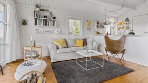 Ett modernt vardagsrum med en vit soffa, ett soffbord och en fåtölj i läder. Det finns en bokhylla fylld med böcker och dekorativa föremål.